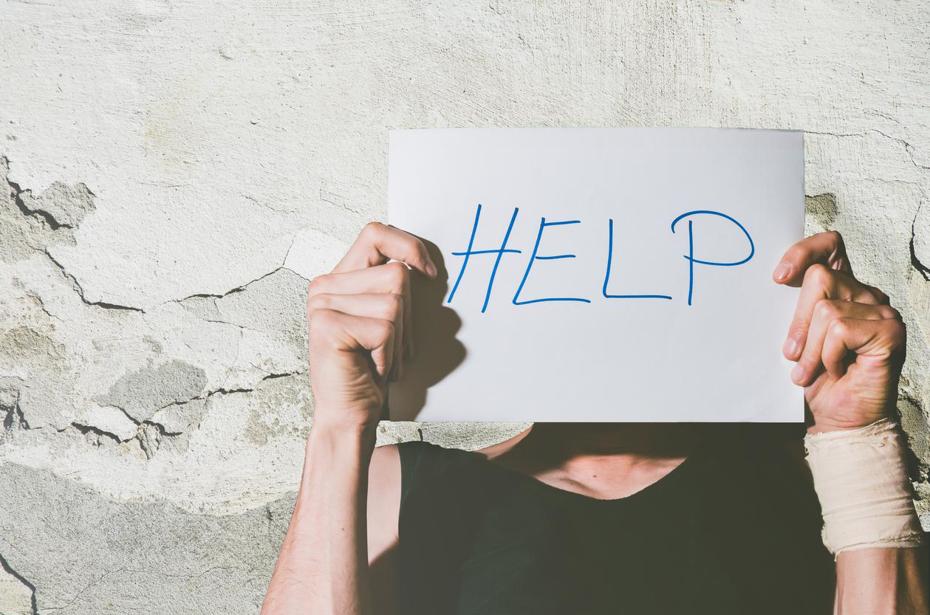 Image of a man holding up a sheet of paper with the word help written across it